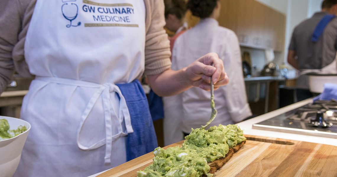 A woman with an apron that reads "GW Culinary Medicine" prepares food