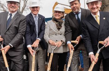 Five people are holding shovels at a ground-breaking ceremony